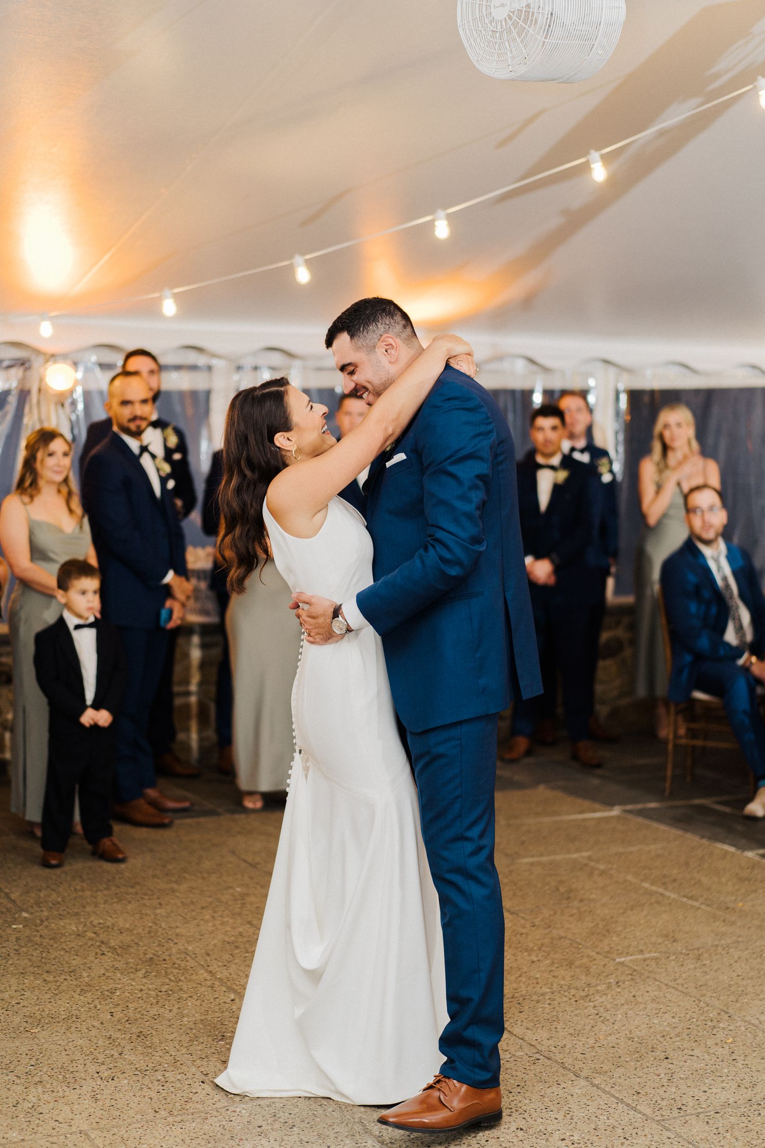 Romantic dance moment under string lights at wedding reception.