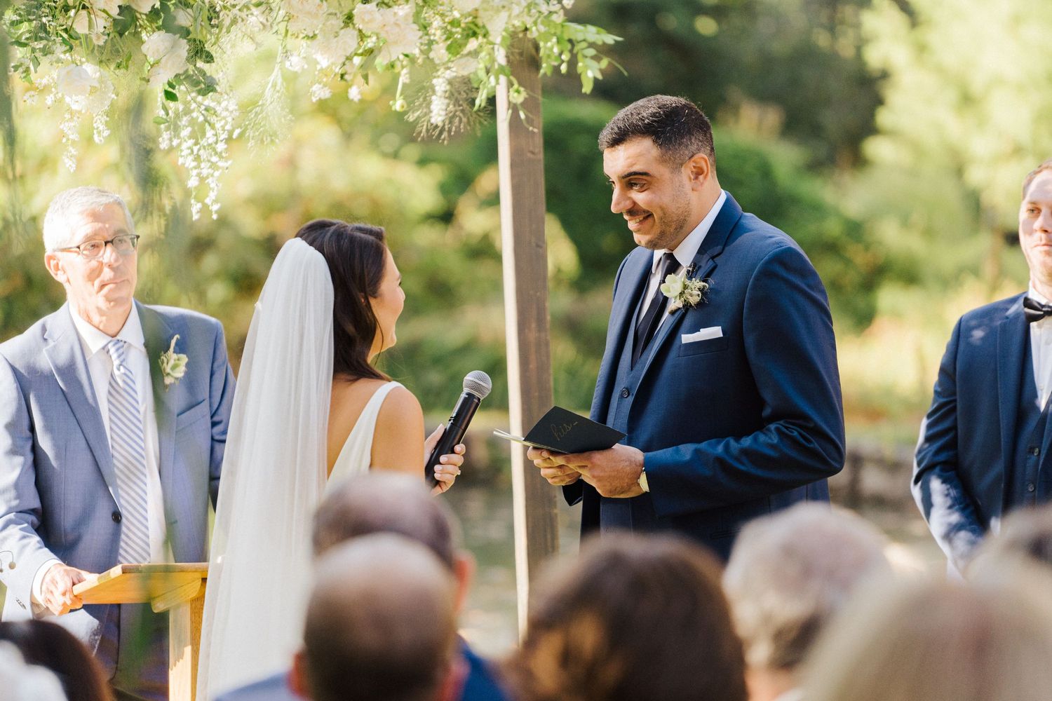 A couple shares their vows beneath flowering trees during an outdoor ceremony.