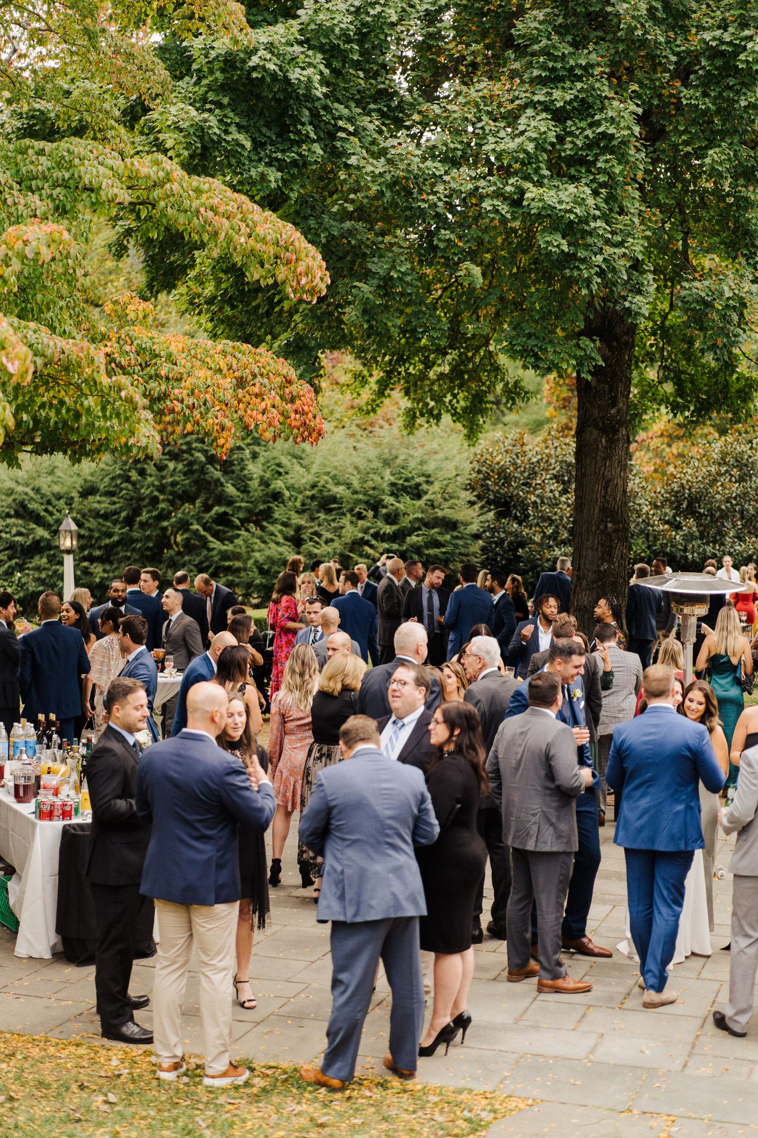 Outdoor wedding reception with guests mingling under autumn trees.