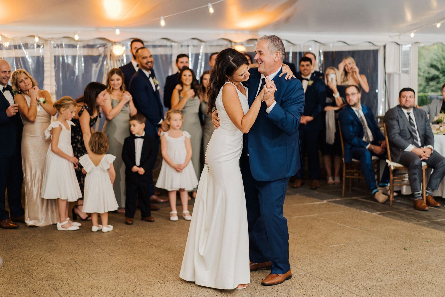 Newlyweds share a romantic dance moment surrounded by wedding guests in a tented reception space.