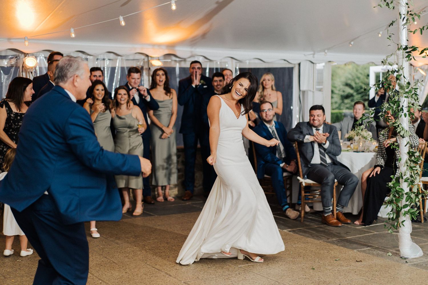 A couple dances elegantly at their wedding reception under string lights in a tent venue.