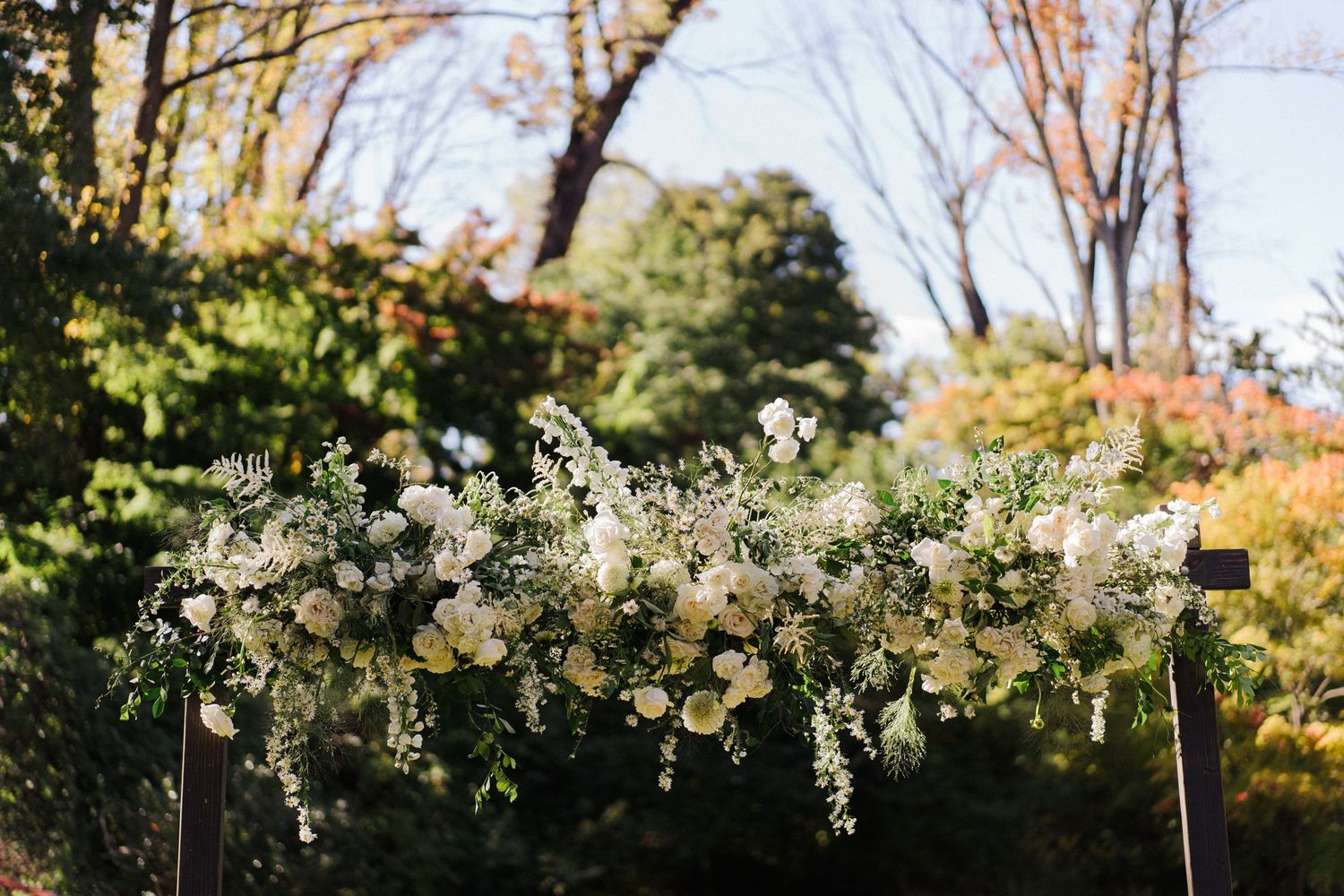 White floral wedding arch arrangement against autumn foliage background.