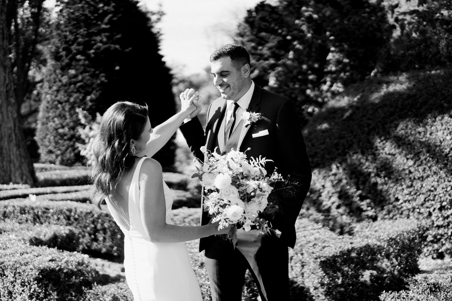 A black and white wedding portrait showing an intimate moment in a formal garden setting.