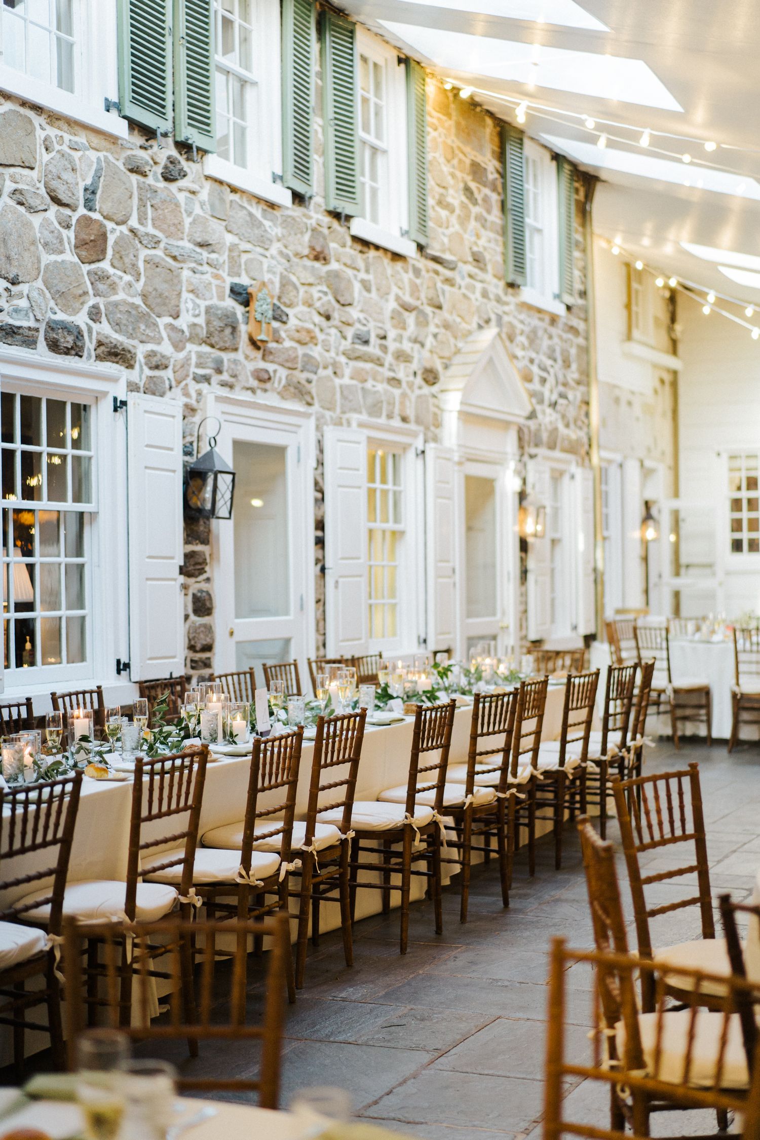 Rustic stone wall dining area set with wooden chiavari chairs for wedding reception.