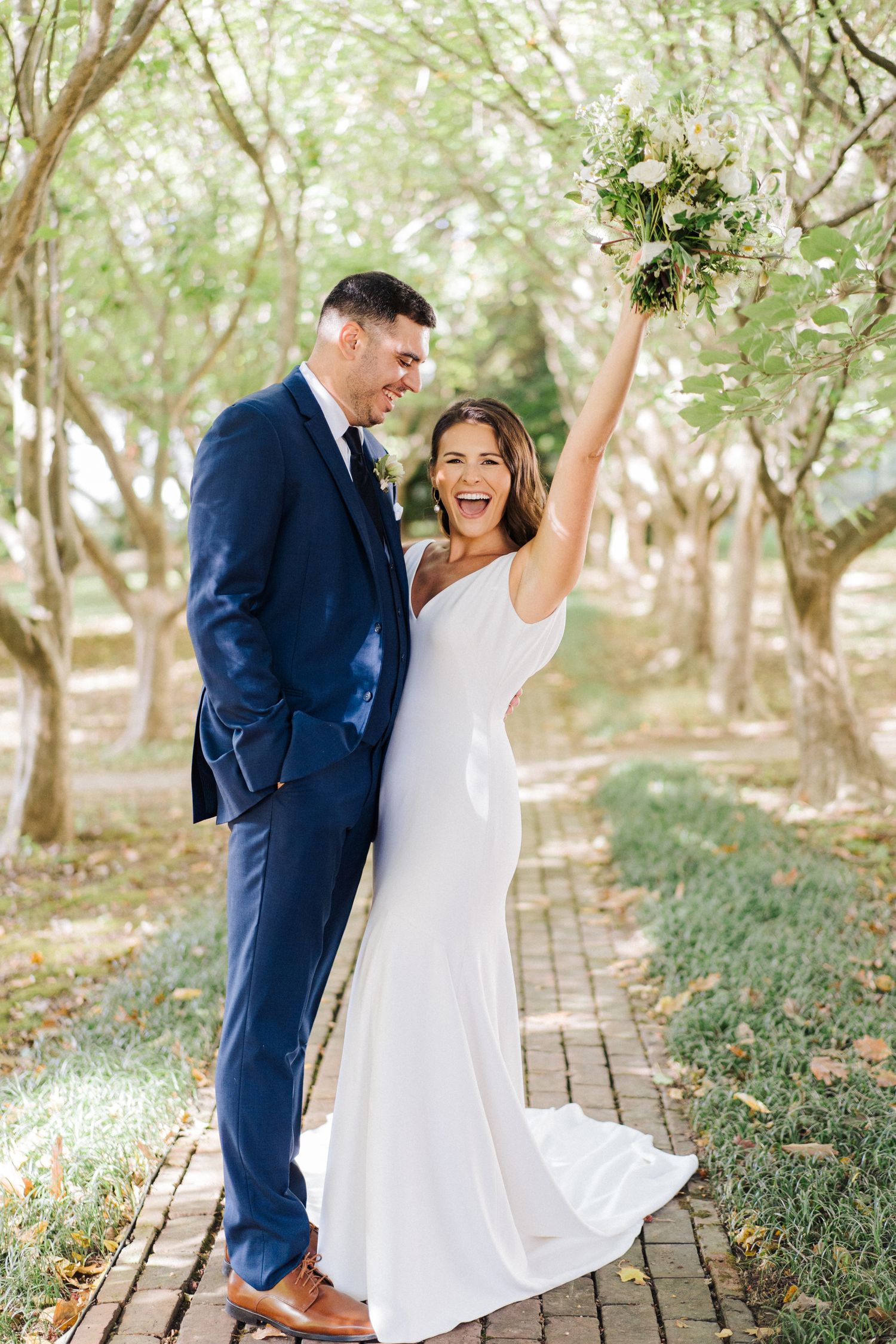 Joyful wedding celebration moment with bouquet raised high on garden path.