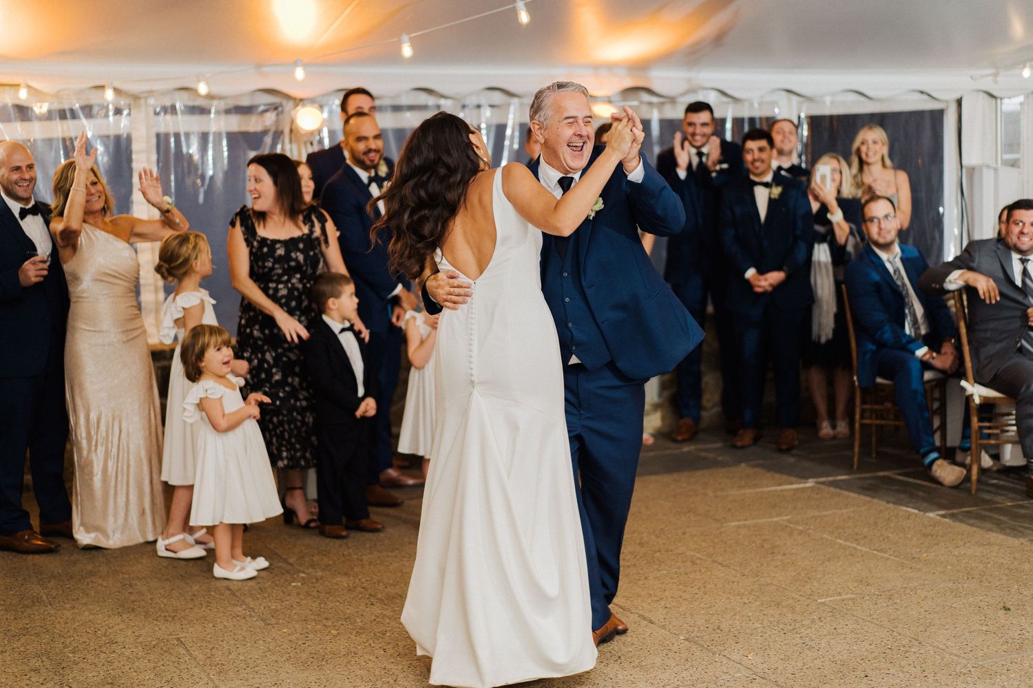 Wedding guests watch as a couple enjoys their dance together under an illuminated tent.