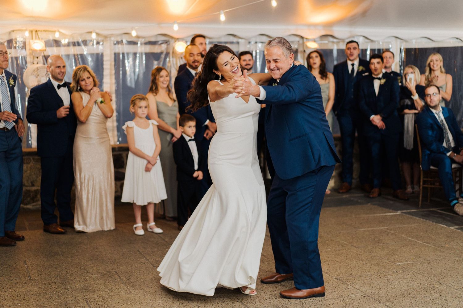 A wedding reception dance under a white tent with guests watching and string lights overhead.