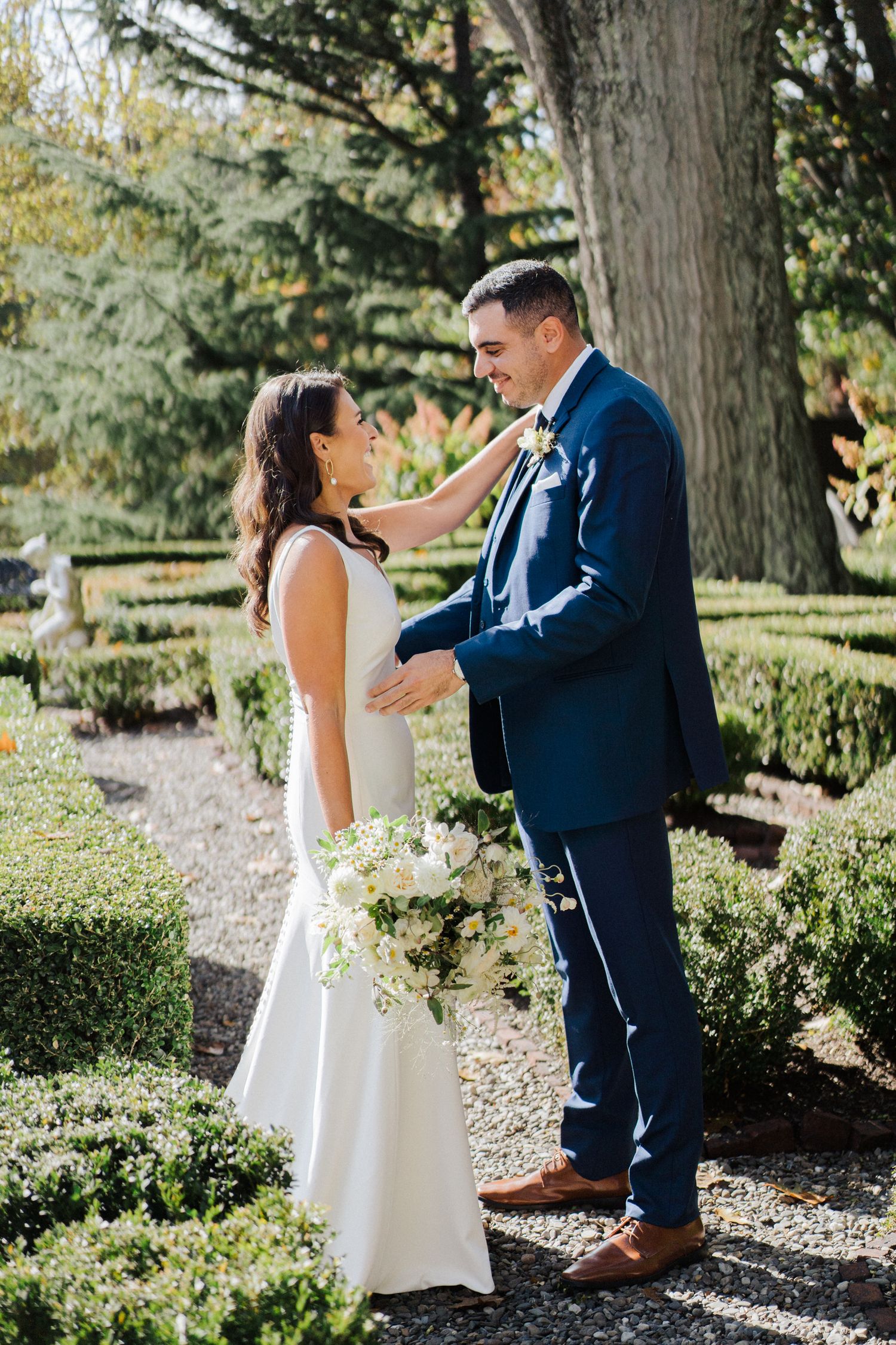 An intimate wedding moment captured on a garden path surrounded by manicured hedges and evergreens.