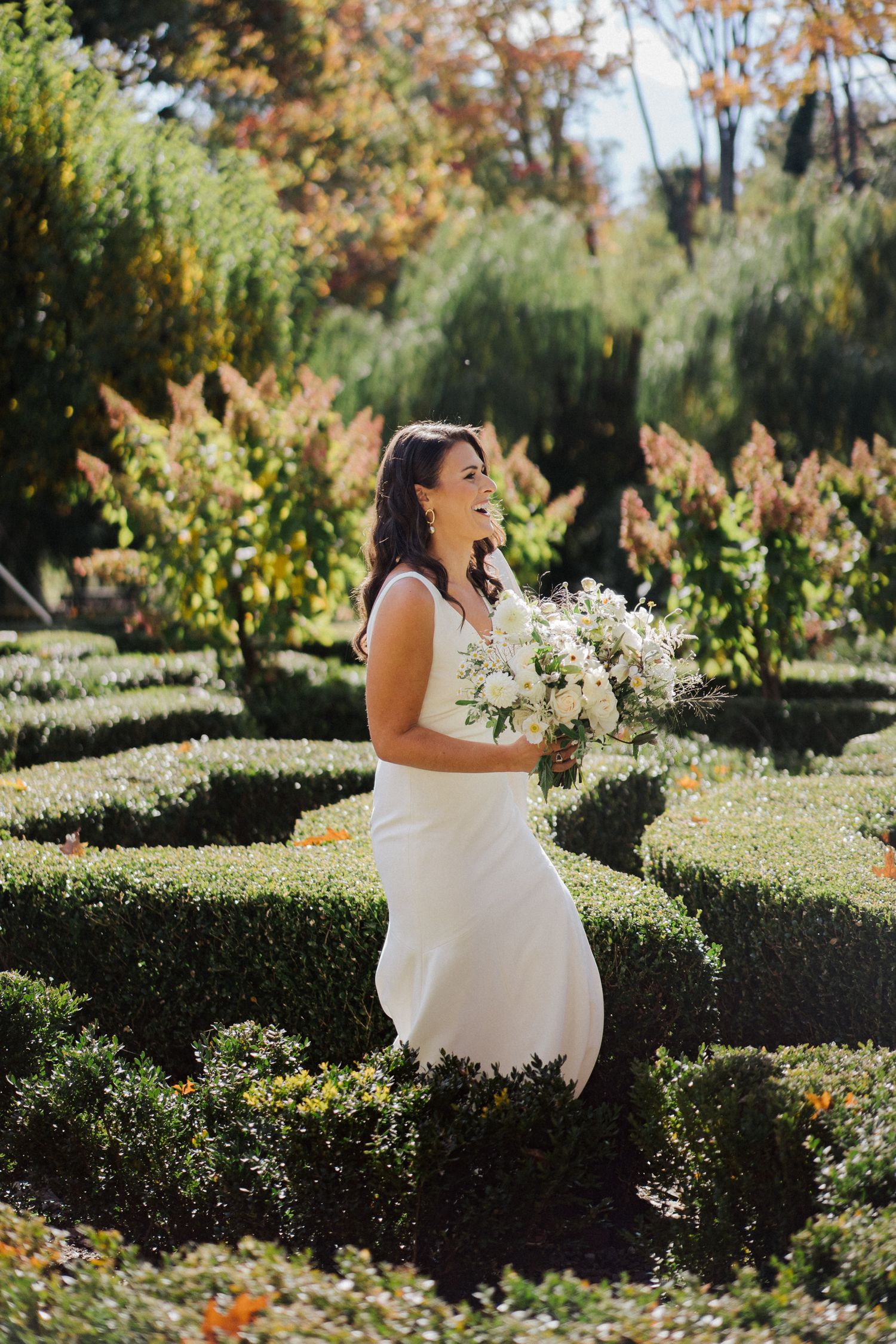 A joyful wedding moment captured in a manicured garden with autumn foliage and ornamental hedges.