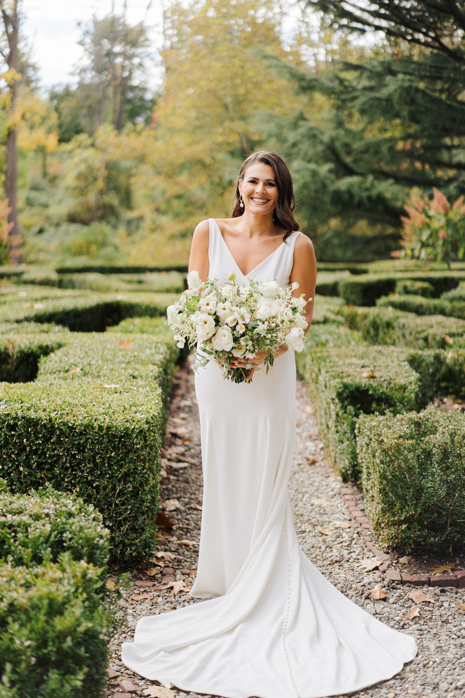 Elegant bridal portrait in garden maze with flowing white dress and bouquet.