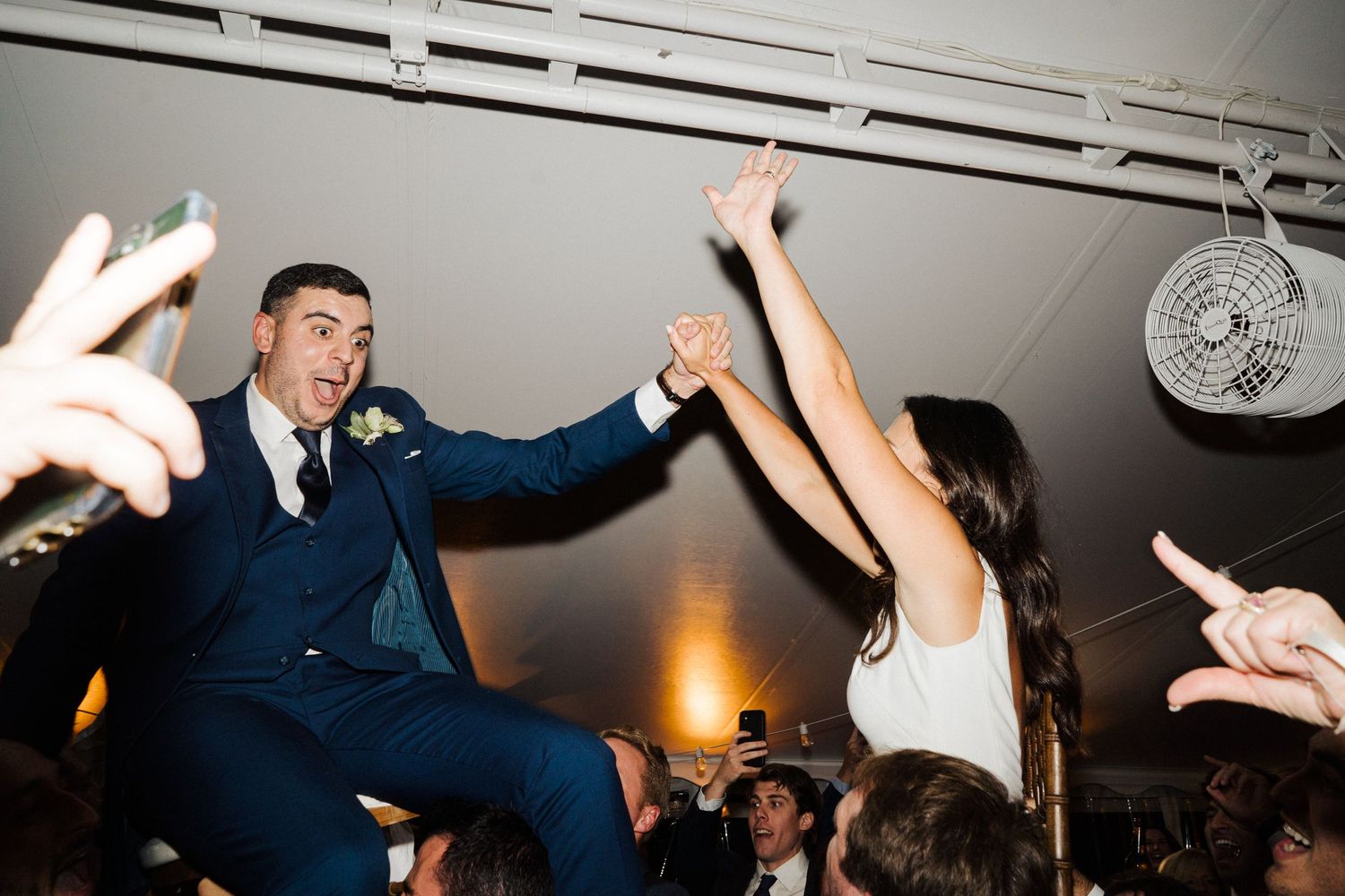 Guests lift a celebrating couple during an energetic wedding reception dance party.