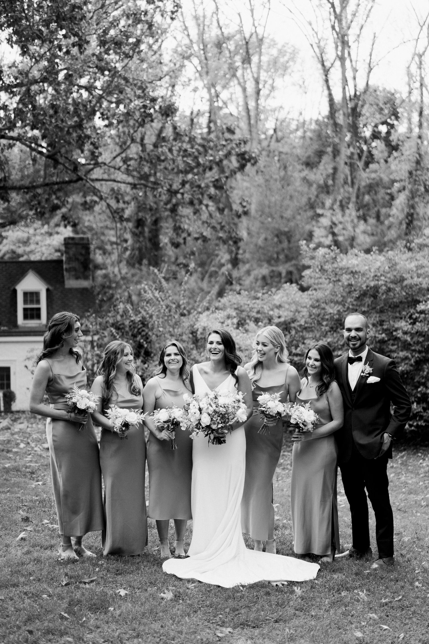 Black and white formal wedding party portrait outdoors with classic house in background.