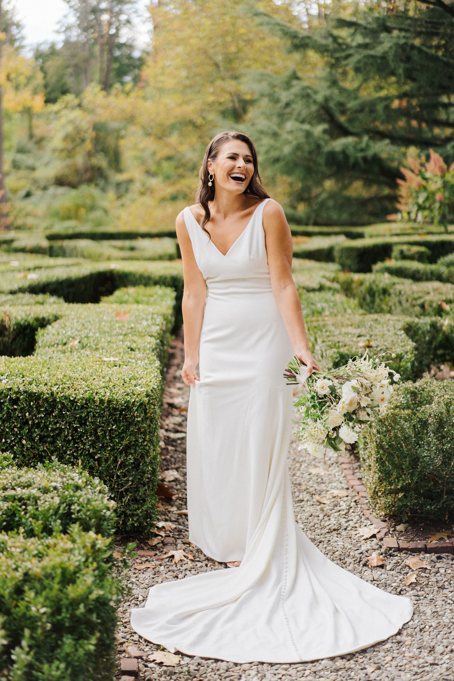 Candid moment of joy in white wedding gown against manicured garden backdrop.