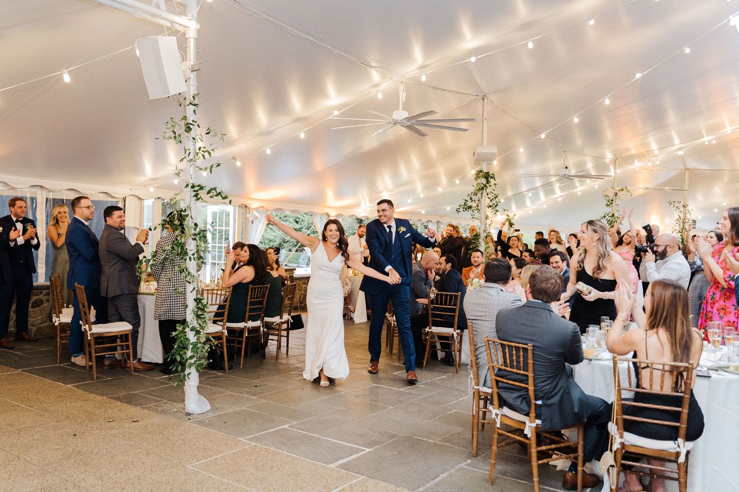 A wedding reception in a white tent with string lights and elegant table settings.