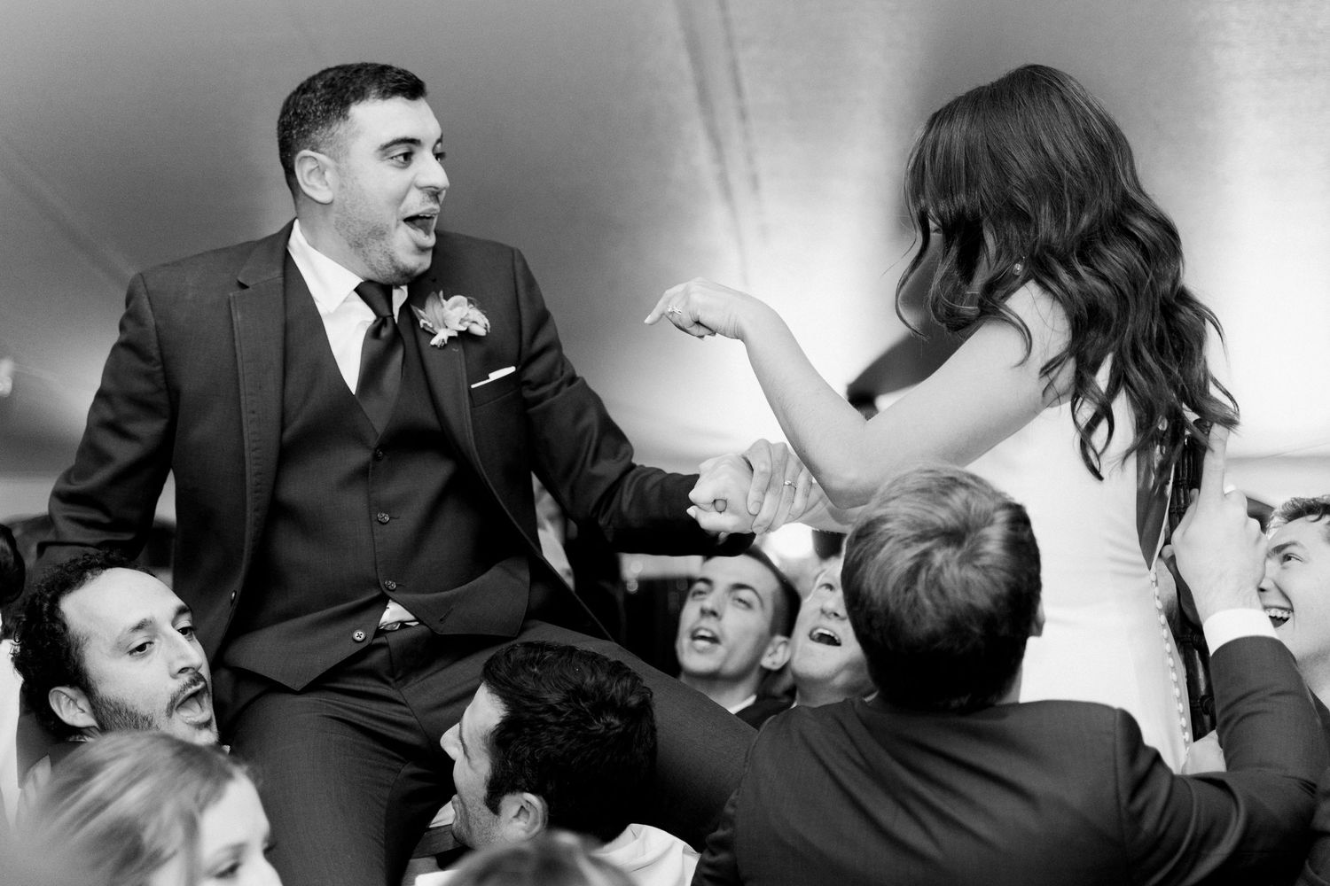 Wedding party lifts groom in celebration during black and white reception photo.