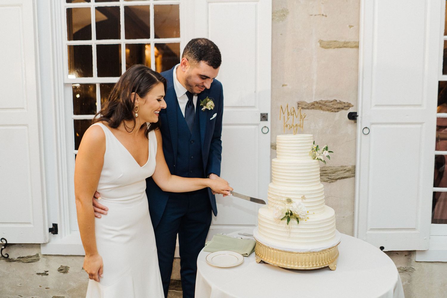 A couple stands beside their elegant white tiered wedding cake during the reception.