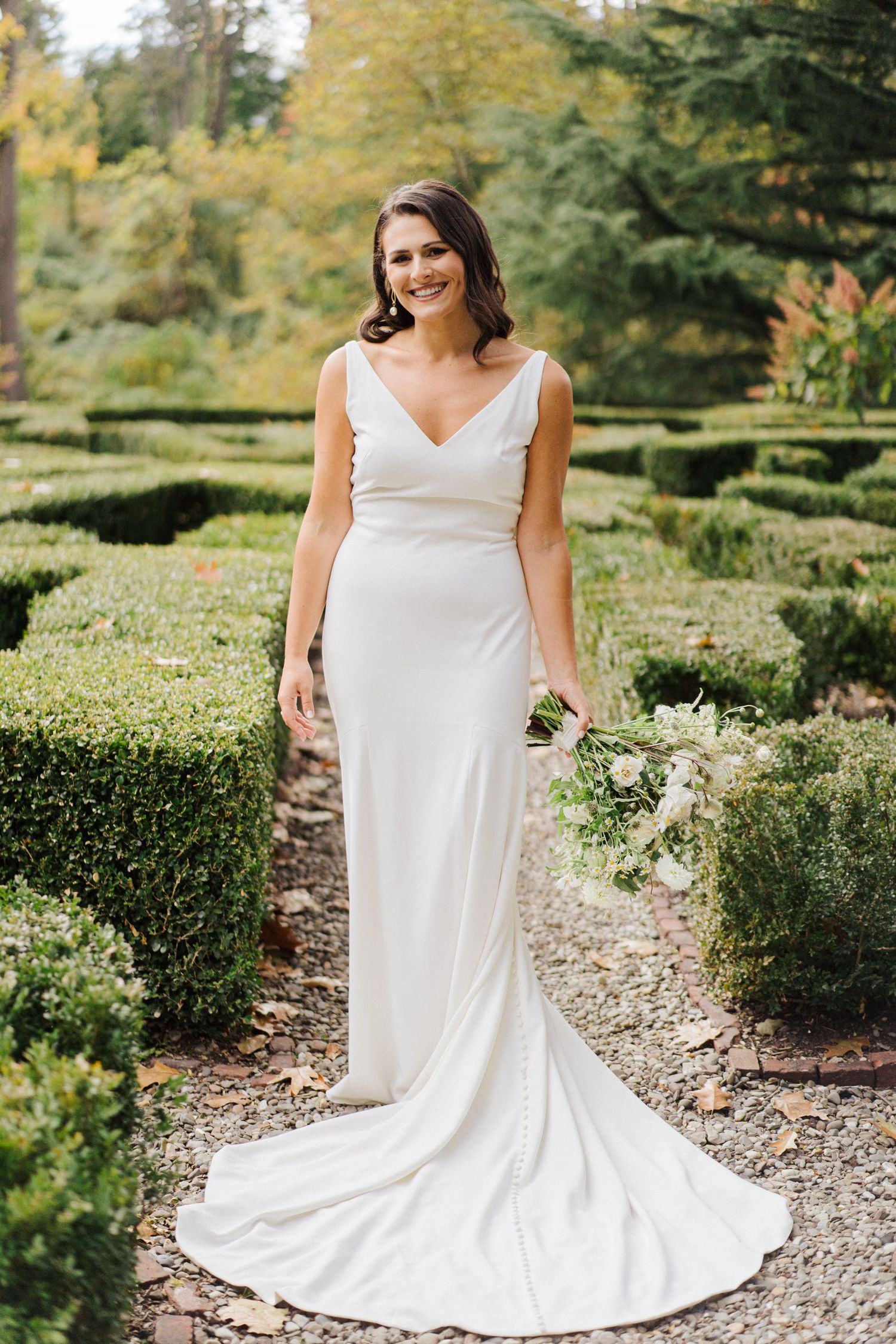 Classic white wedding dress with v-neck and train in formal garden setting.