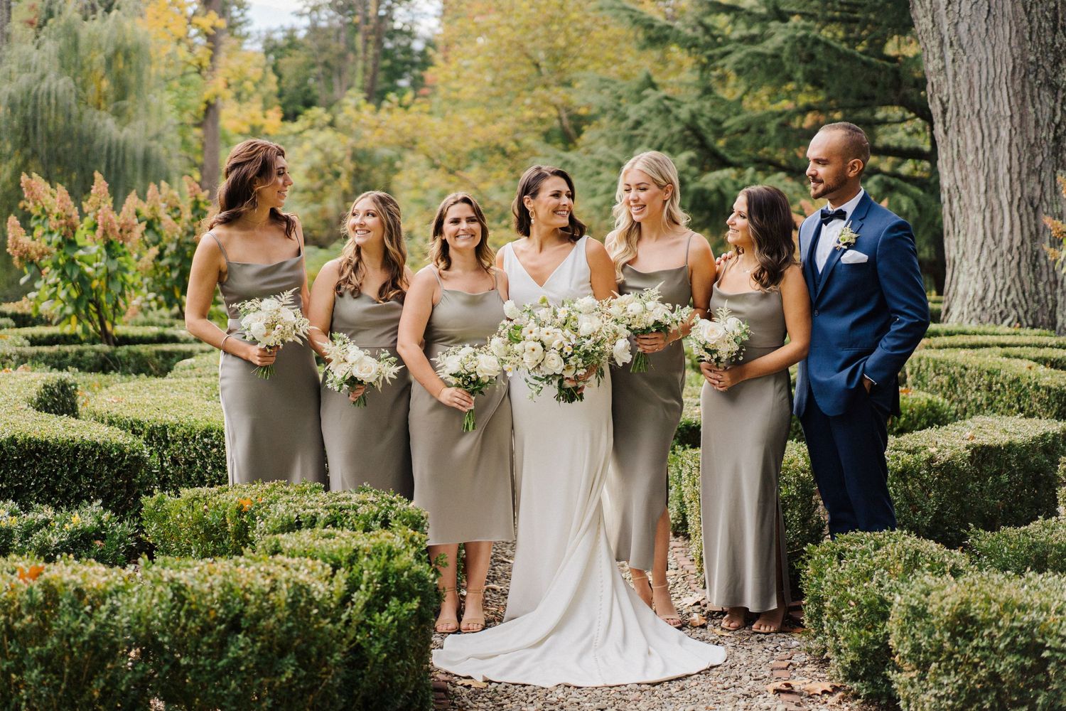 Wedding group standing on garden path surrounded by ornamental hedges in autumn.