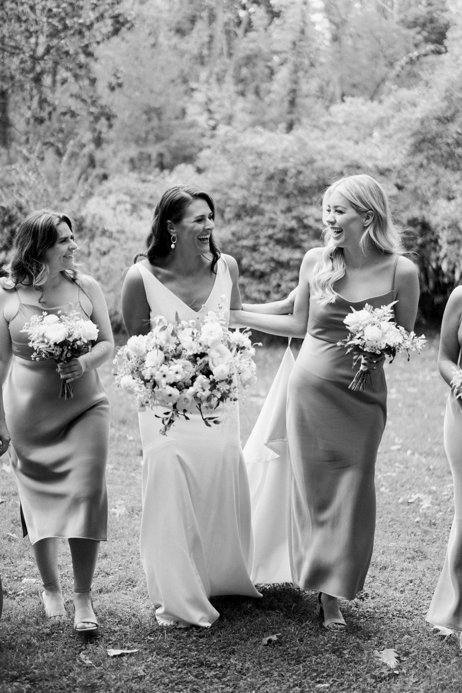 Black and white candid moment between wedding party members holding bouquets outdoors.
