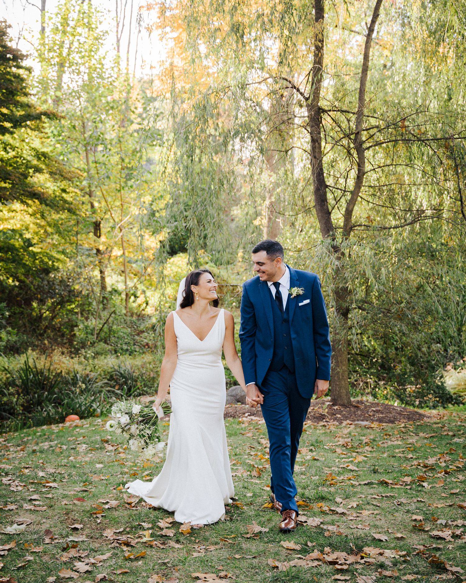 A couple walks together on an autumn day in a garden with willow trees.