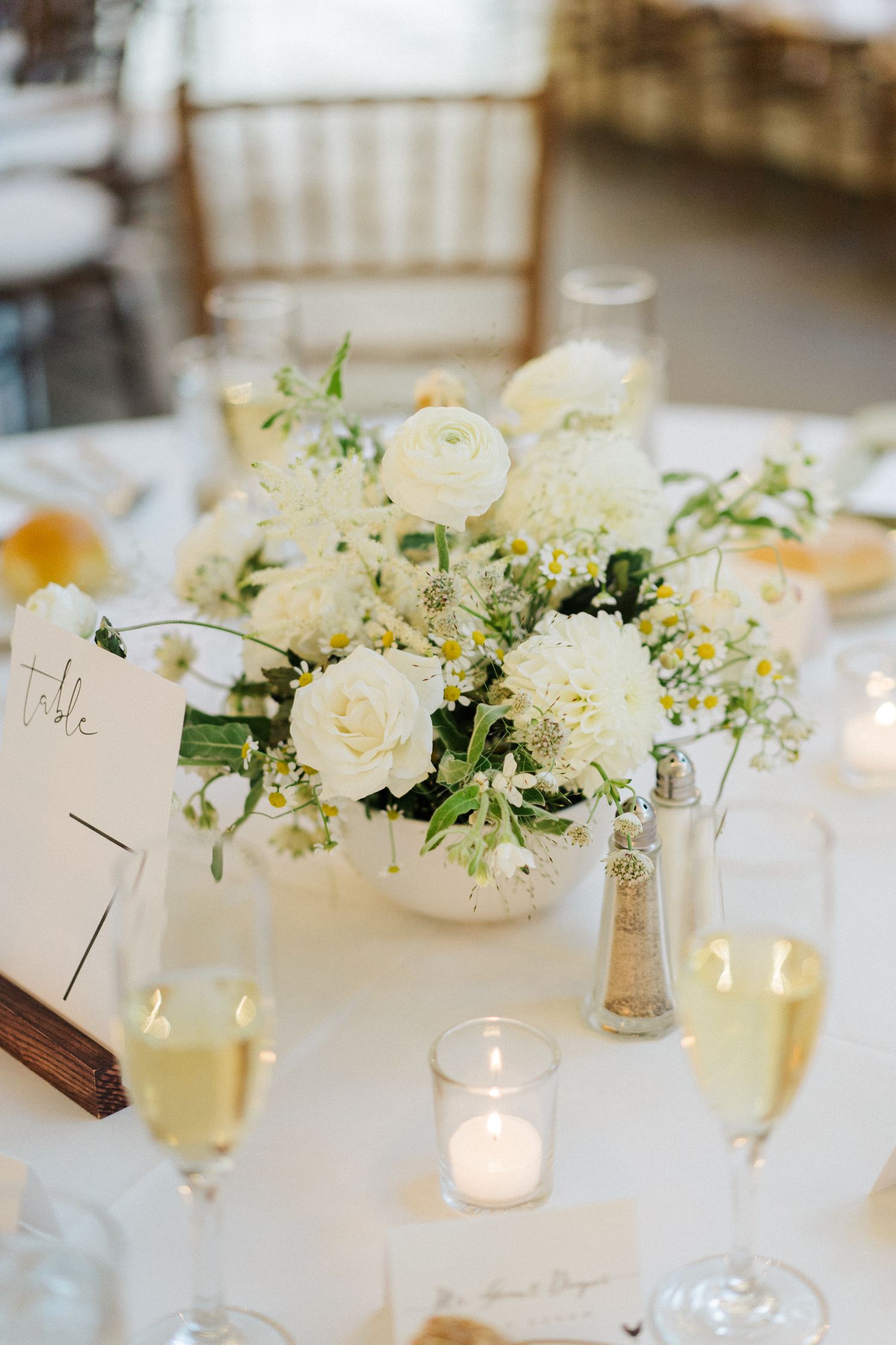 Elegant white rose centerpiece with candles on wedding reception table.