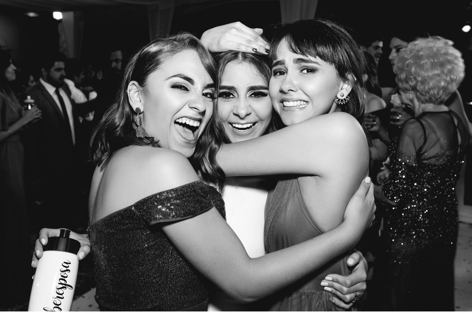 Three friends share a joyful embrace at an elegant evening celebration.