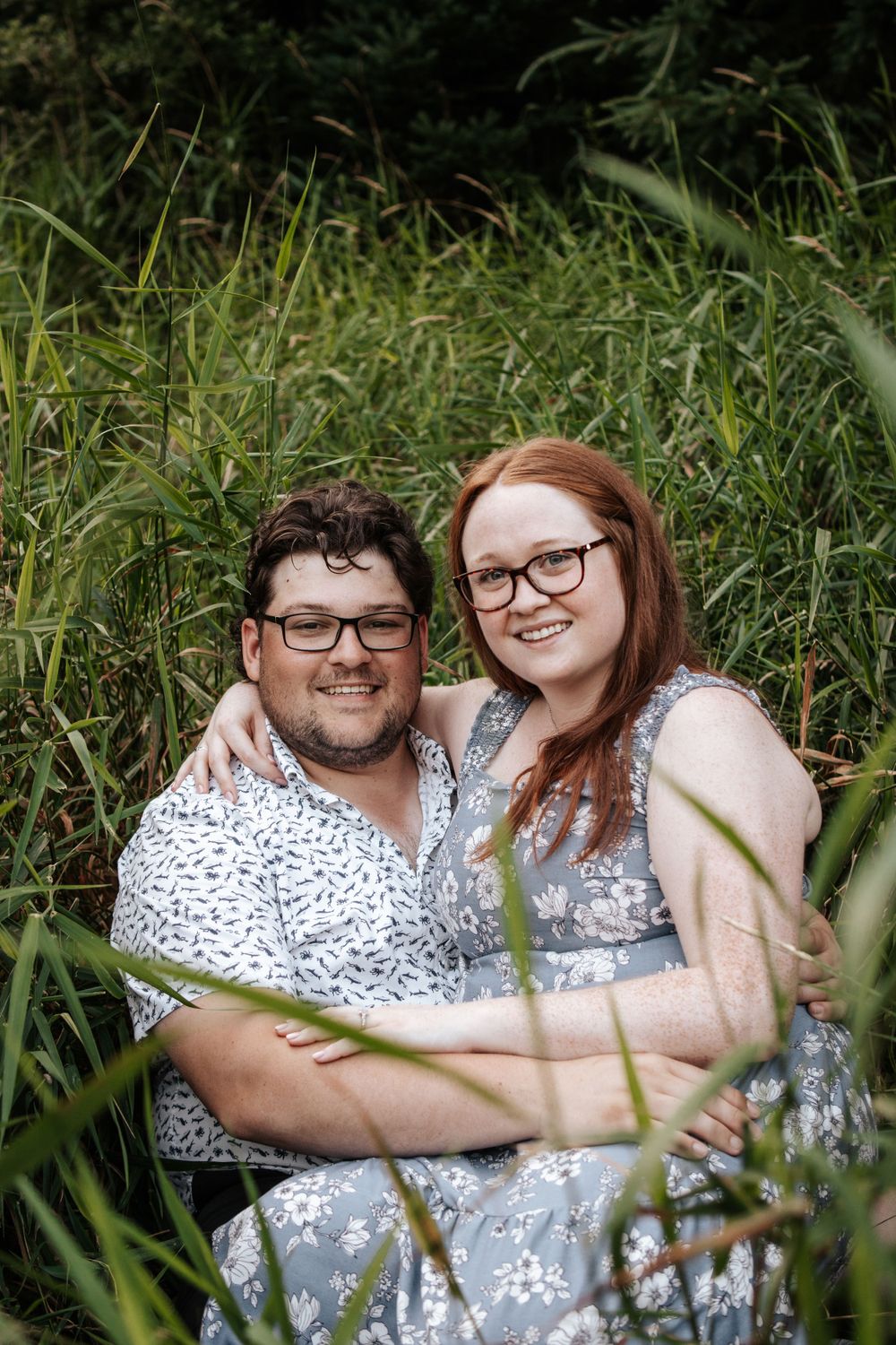 A cheerful couple sits together in tall grass on a summer day.