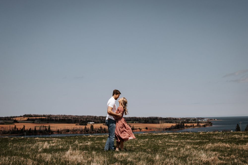 A couple embraces in a playful lift pose on a scenic coastal clifftop. Photo at Carriage House New London PEI