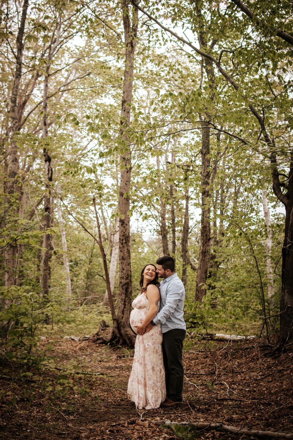 An expecting couple poses together in a dreamy forest setting.