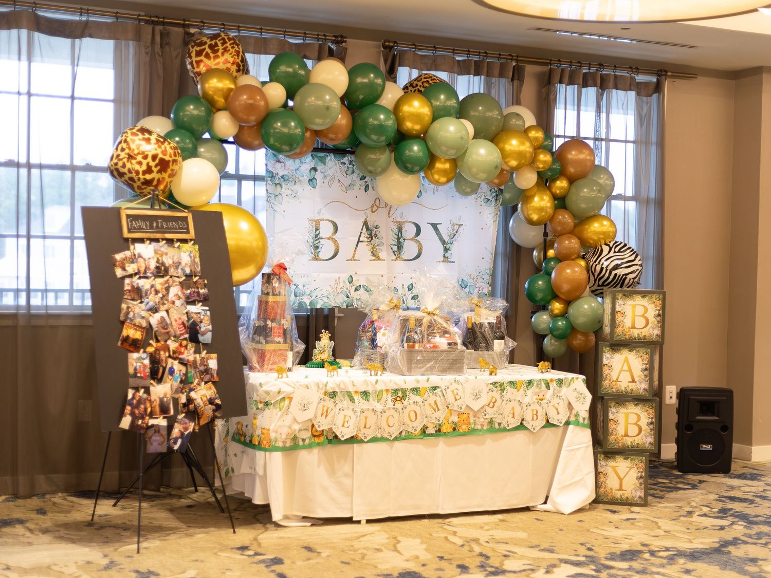 Baby shower venue decorated with elegant gold and green balloon arches and white furniture.