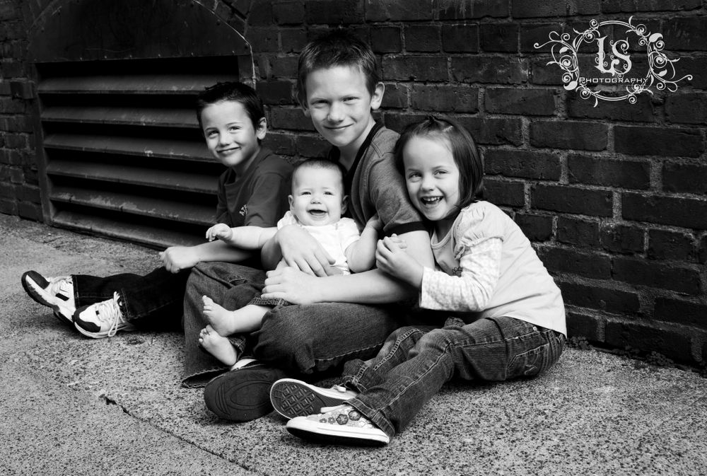 Children relaxing against brick wall in casual black and white portrait.