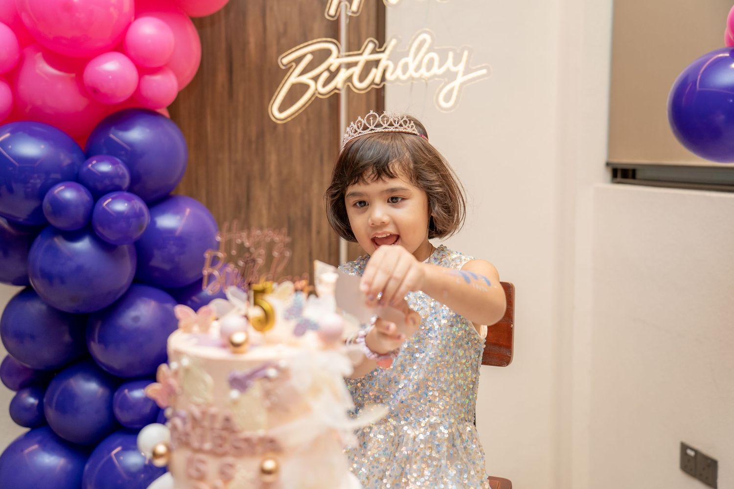 A birthday party with purple and pink balloon arch decorations and a sparkly cake.