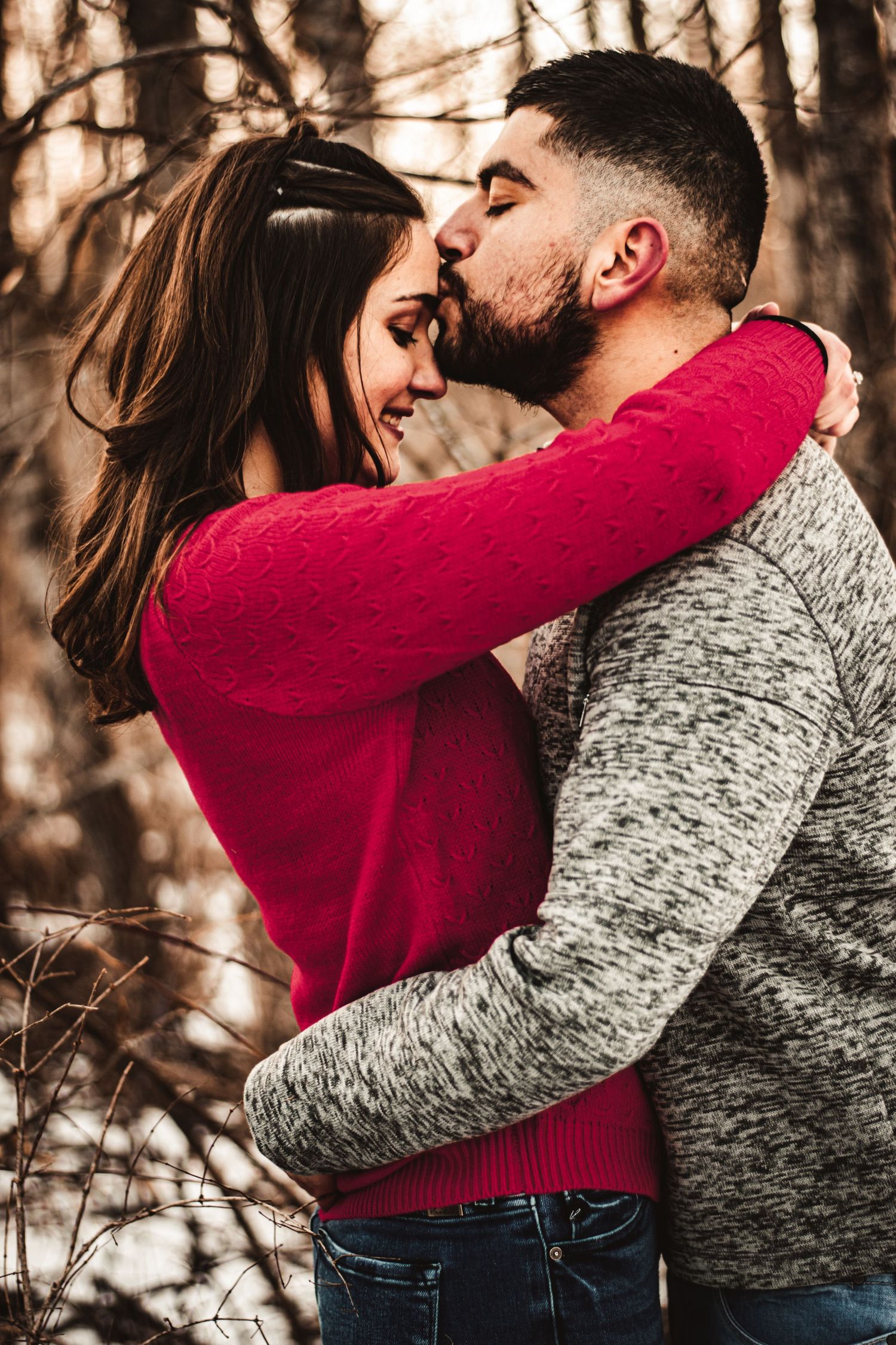 A romantic winter embrace between a couple in red and grey sweaters against a forest backdrop.