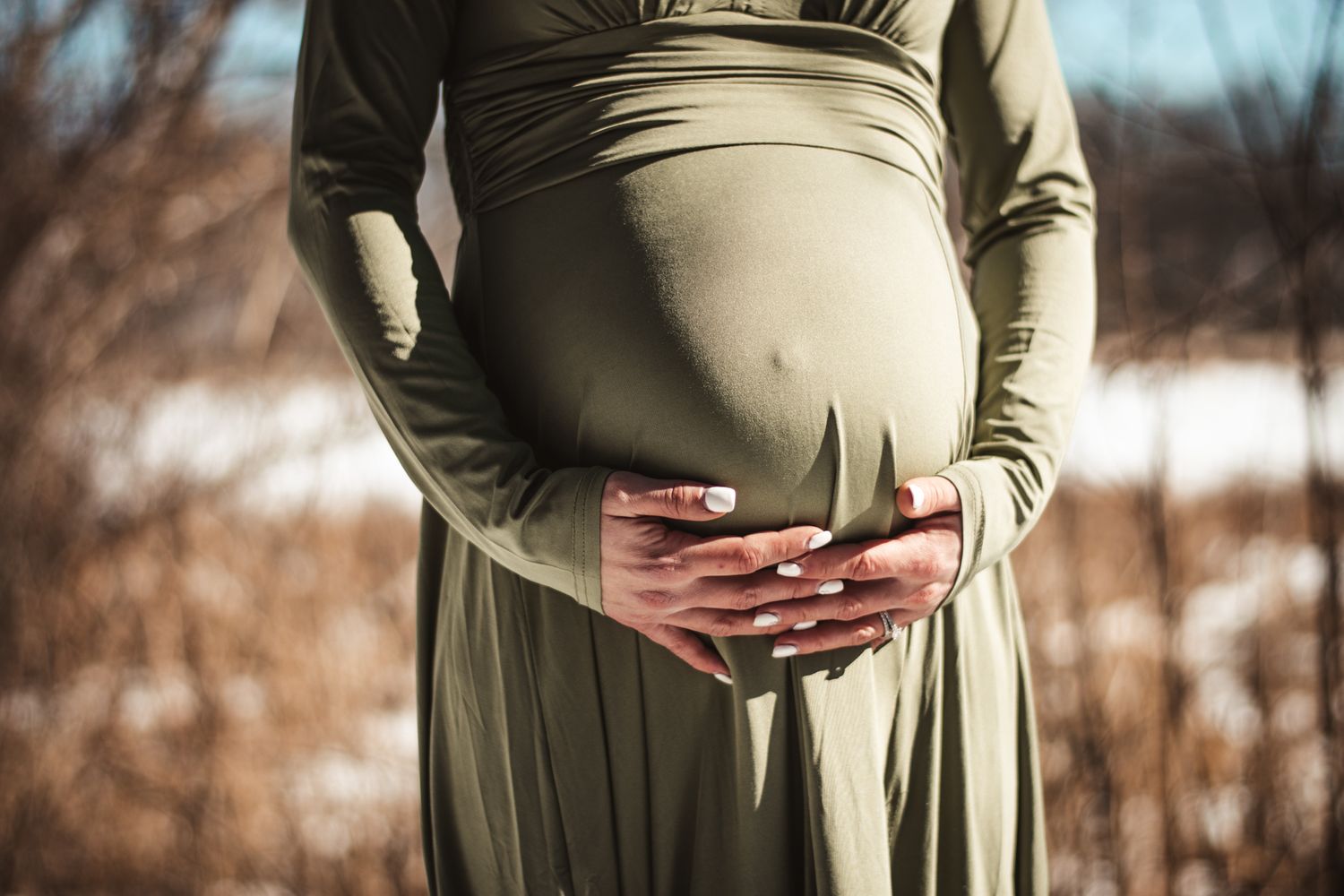 Close-up of hands cradling a pregnant belly in an olive green maternity dress.