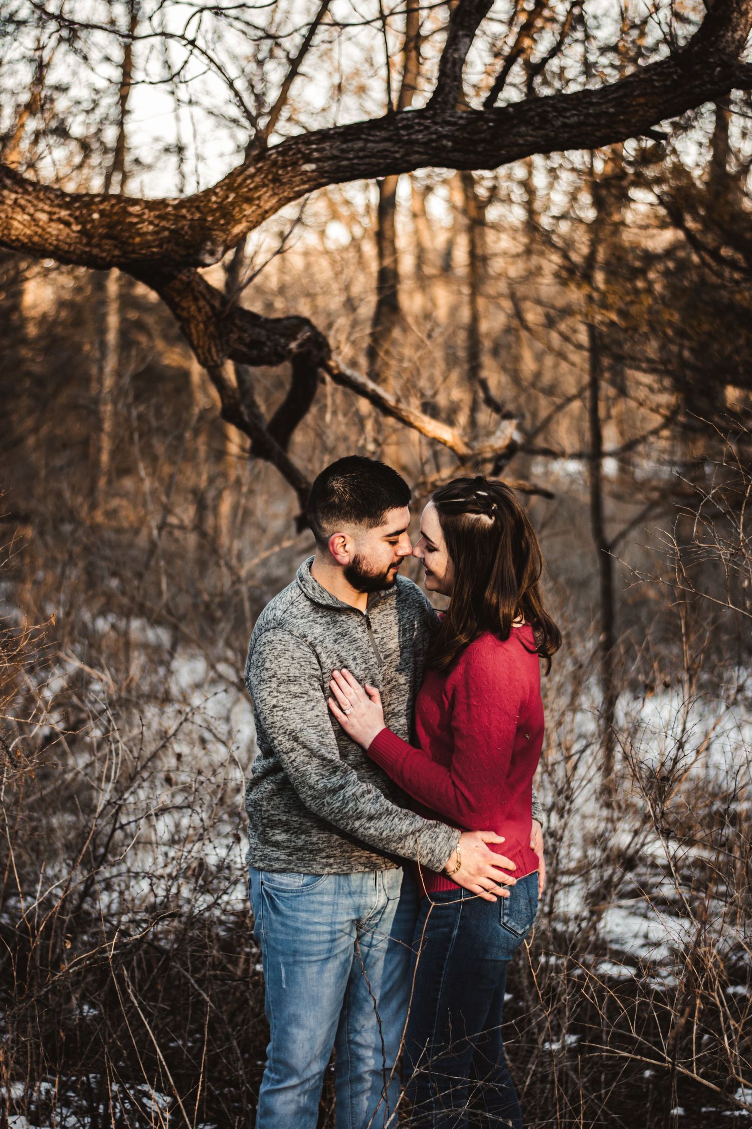An intimate moment shared between a couple in the snowy woods under a twisted tree branch.