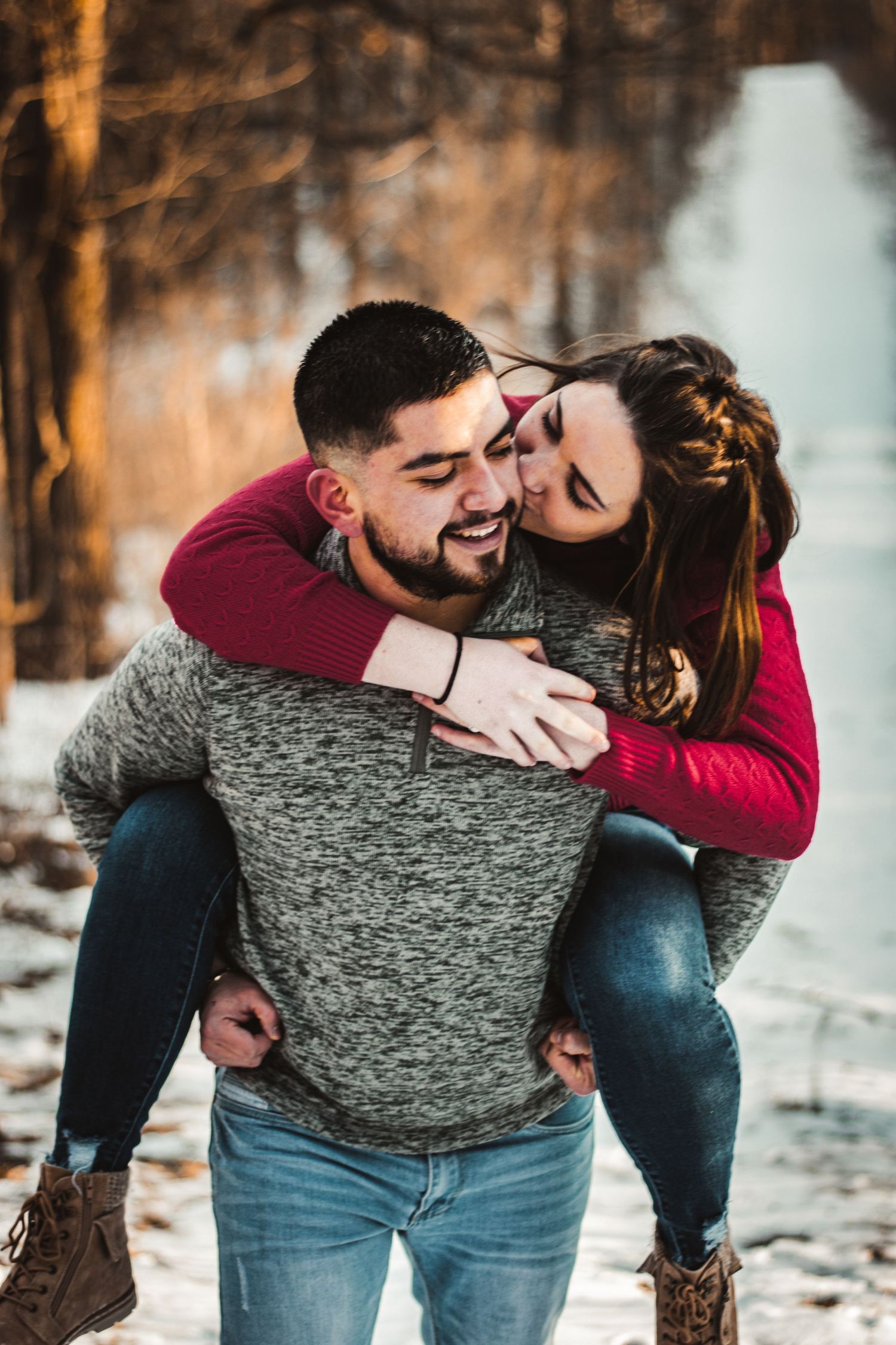 Playful piggyback ride between a couple wearing matching red and grey sweaters in the snow.