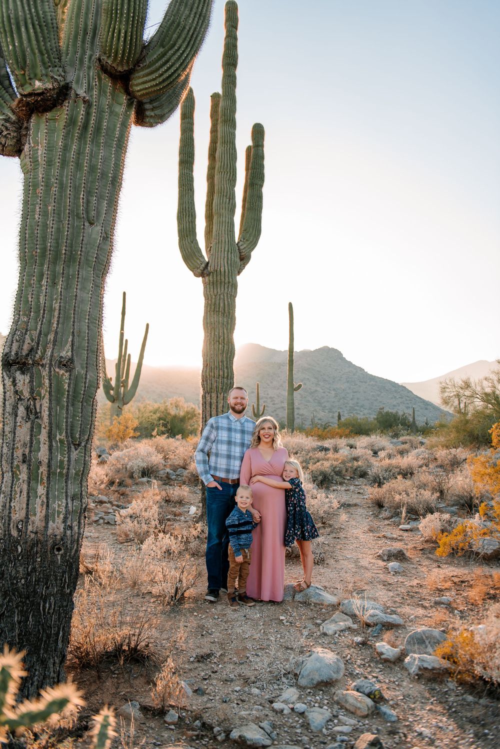 Desert photoshoot featuring a couple standing beside massive saguaro cactus at sunset.