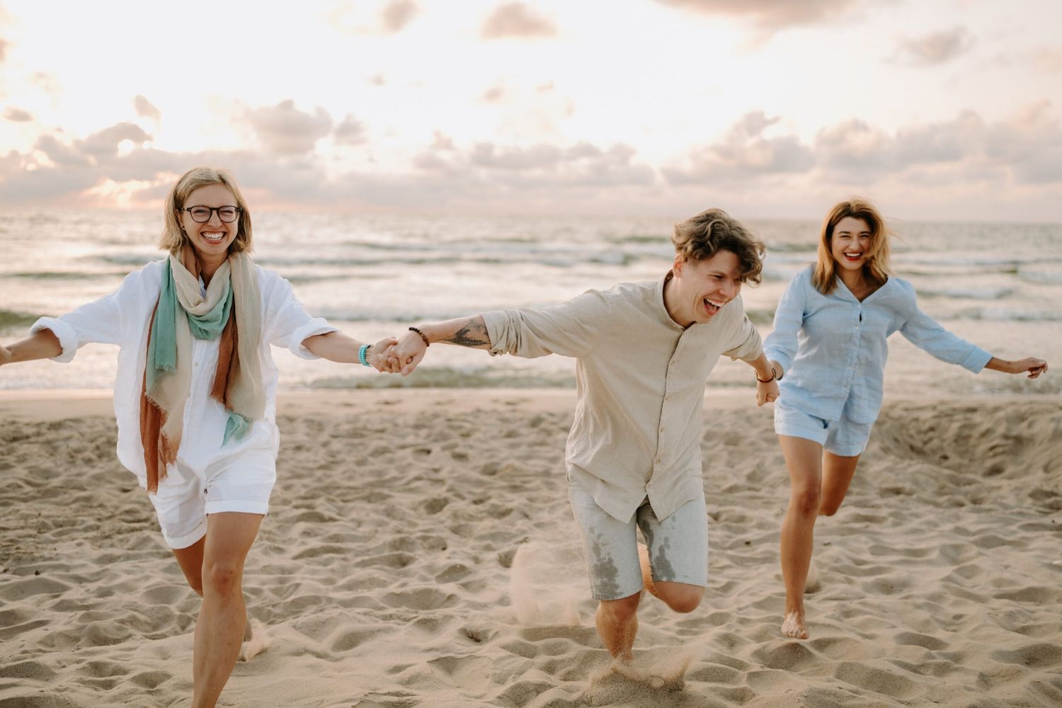 Three friends playing and jumping on the beach at sunset.
