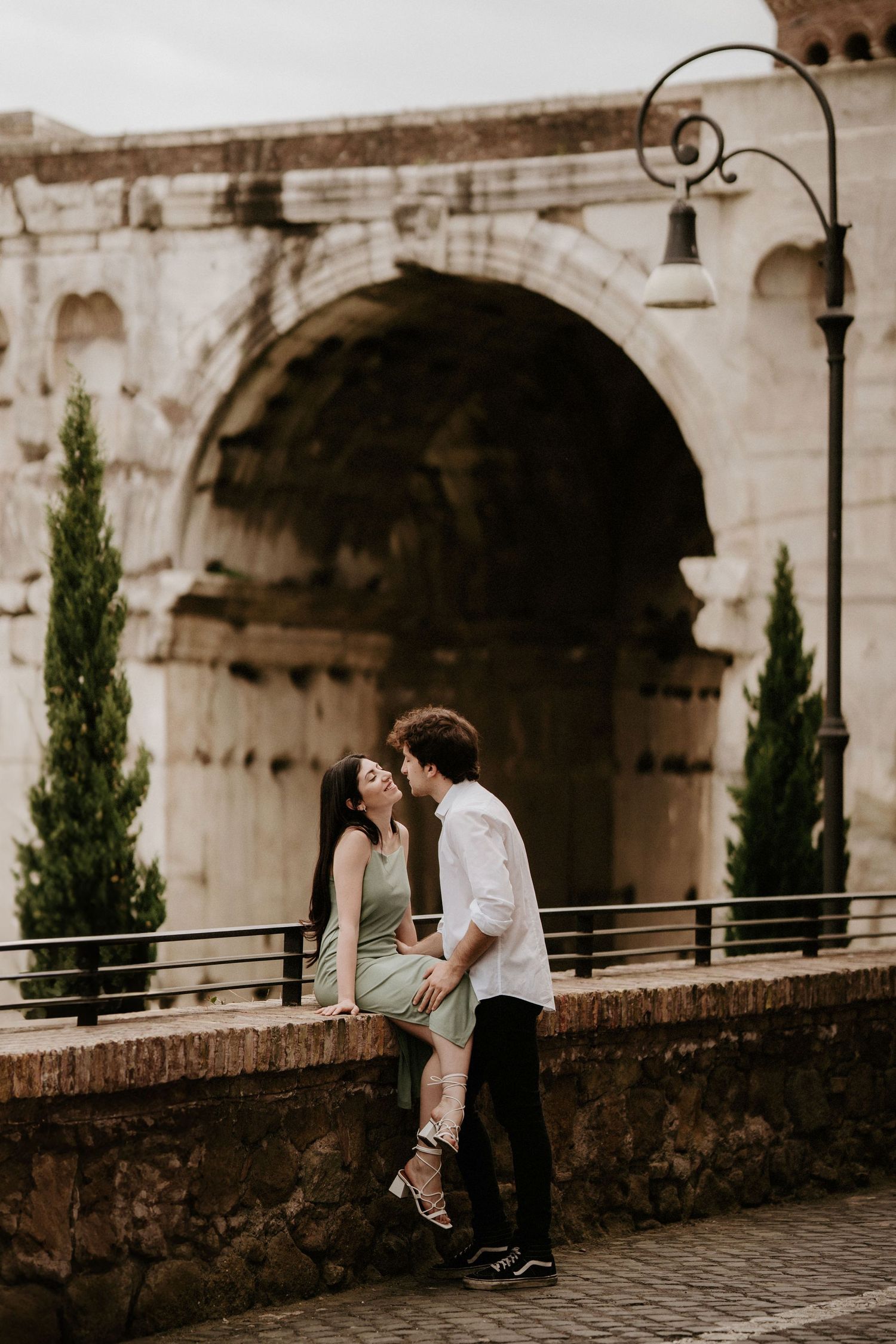 Romantic couple shares intimate moments under historic stone archways at sunset.
