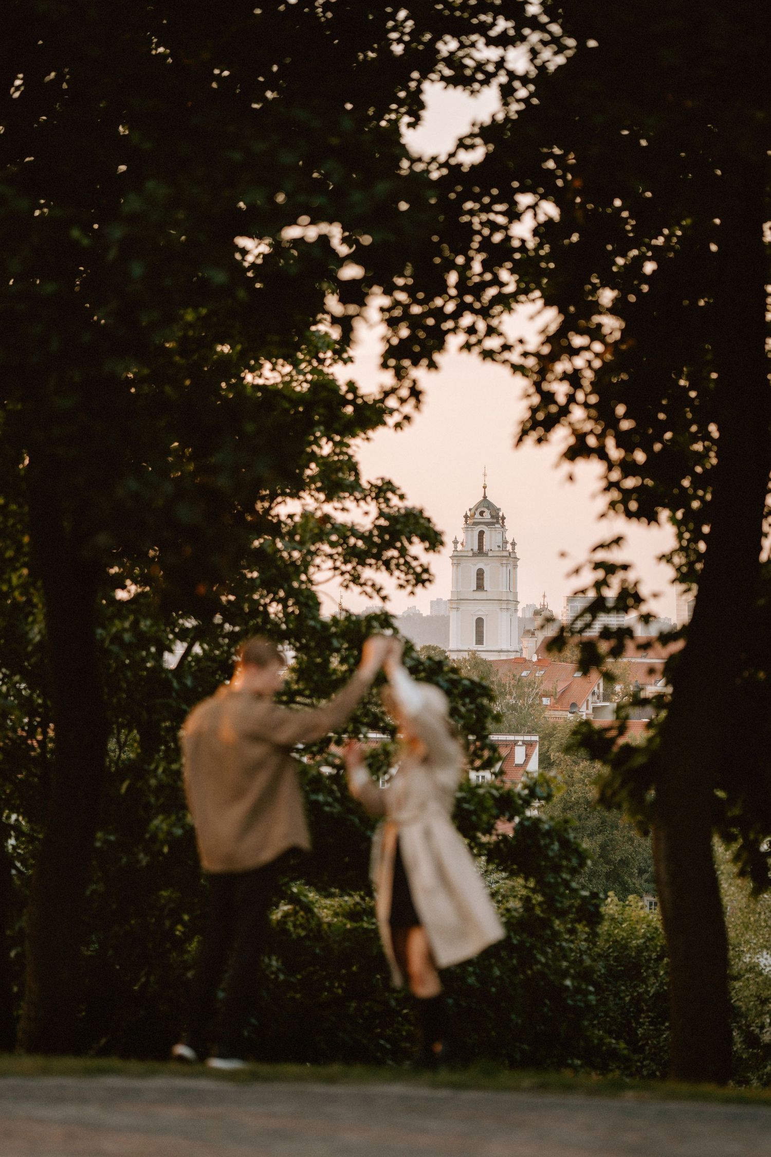 Church steeple visible through trees at sunset with blurred figures in foreground.
