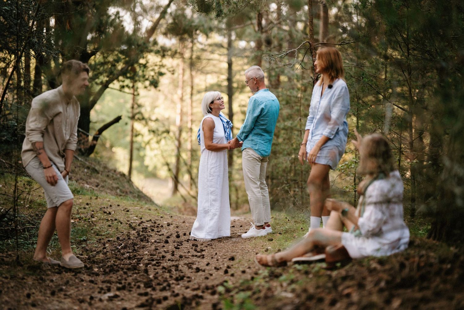 A group gathering in casual attire on a wooded hillside during golden hour.