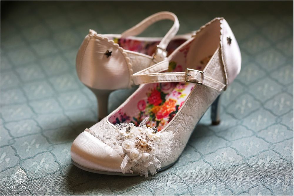 Vintage-style blush wedding shoes with delicate lace details on patterned background.