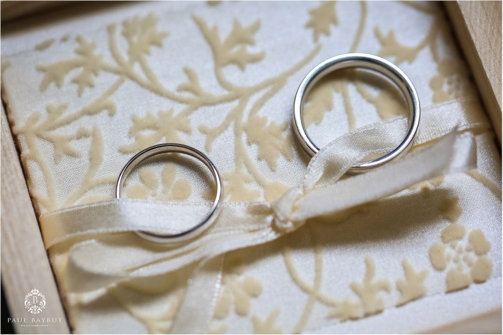 Two silver wedding rings photographed on cream textured paper with floral pattern.