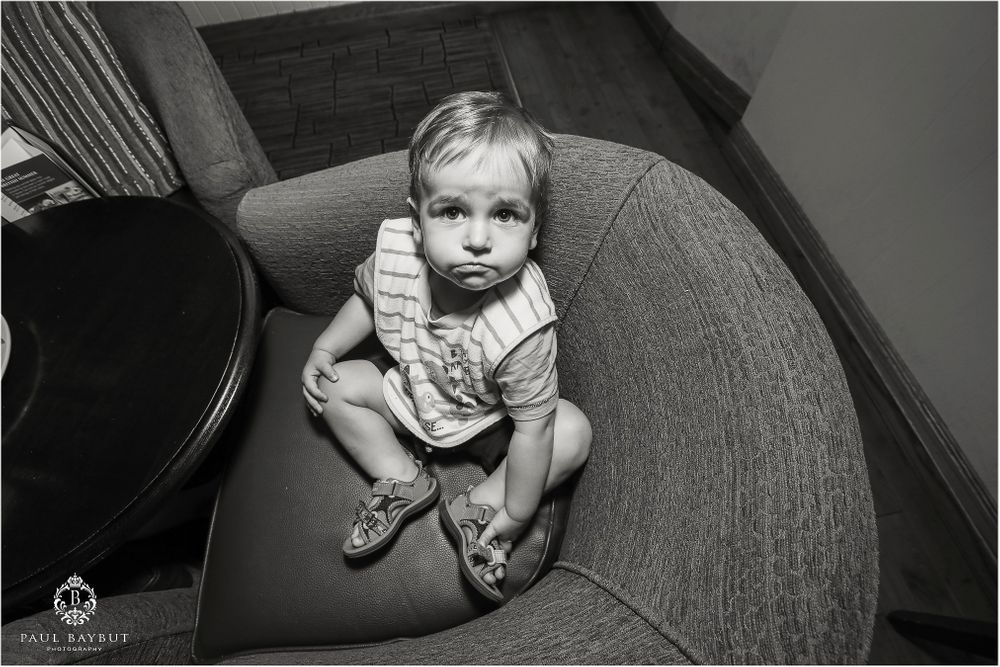 A small child sits curled up on a grey armchair in black and white.