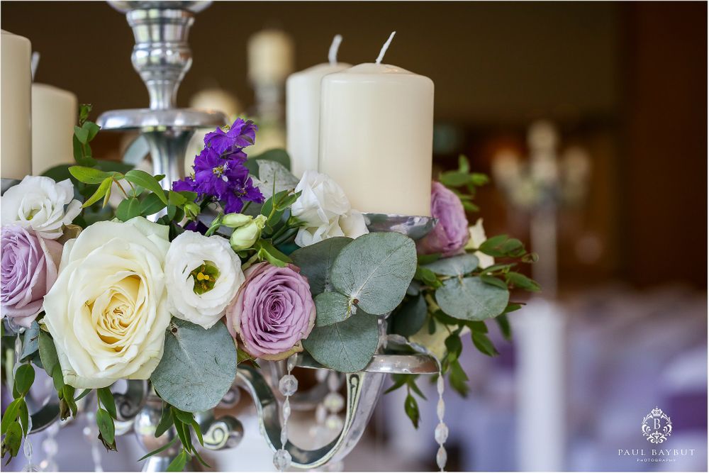 Elegant wedding centerpiece with white and purple roses, eucalyptus leaves, and white candles.