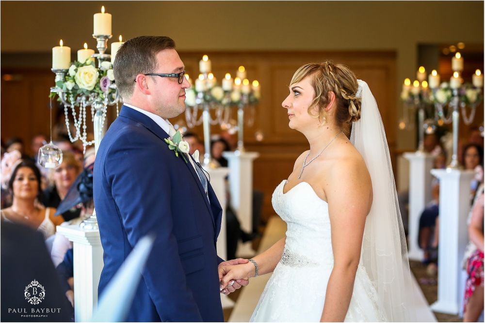 Couple exchanges vows during indoor ceremony with elegant candelabra lighting.