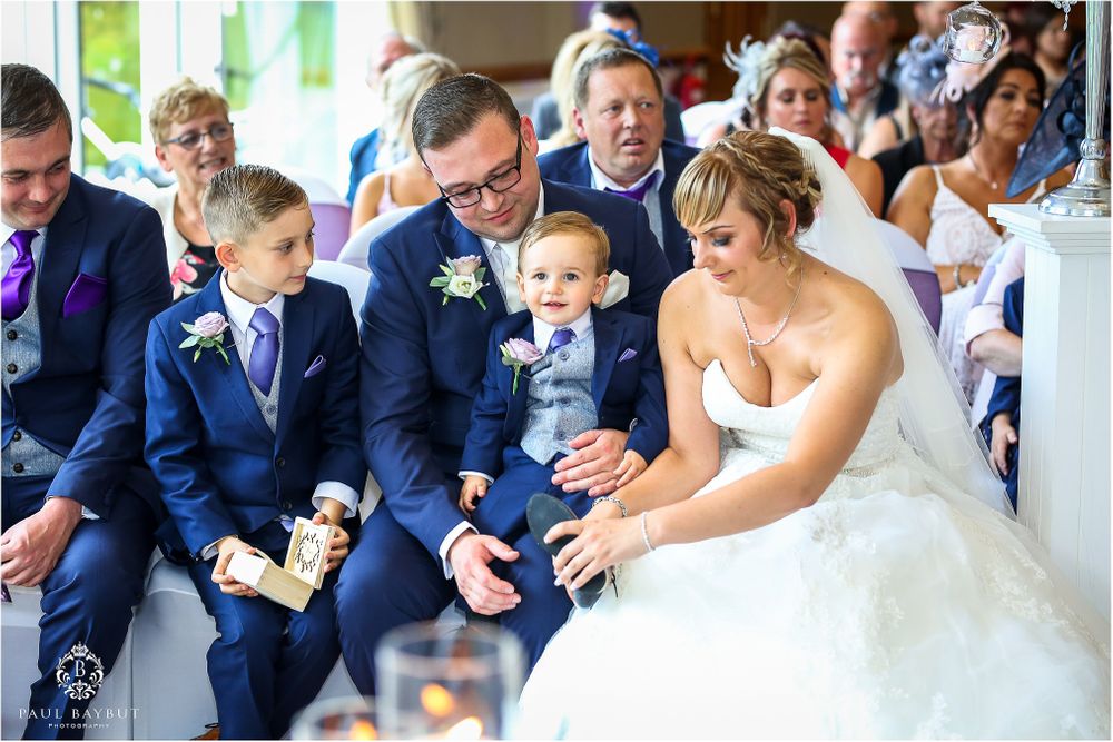 Wedding guests in formal attire watching a tender moment during a wedding ceremony in an elegant venue.