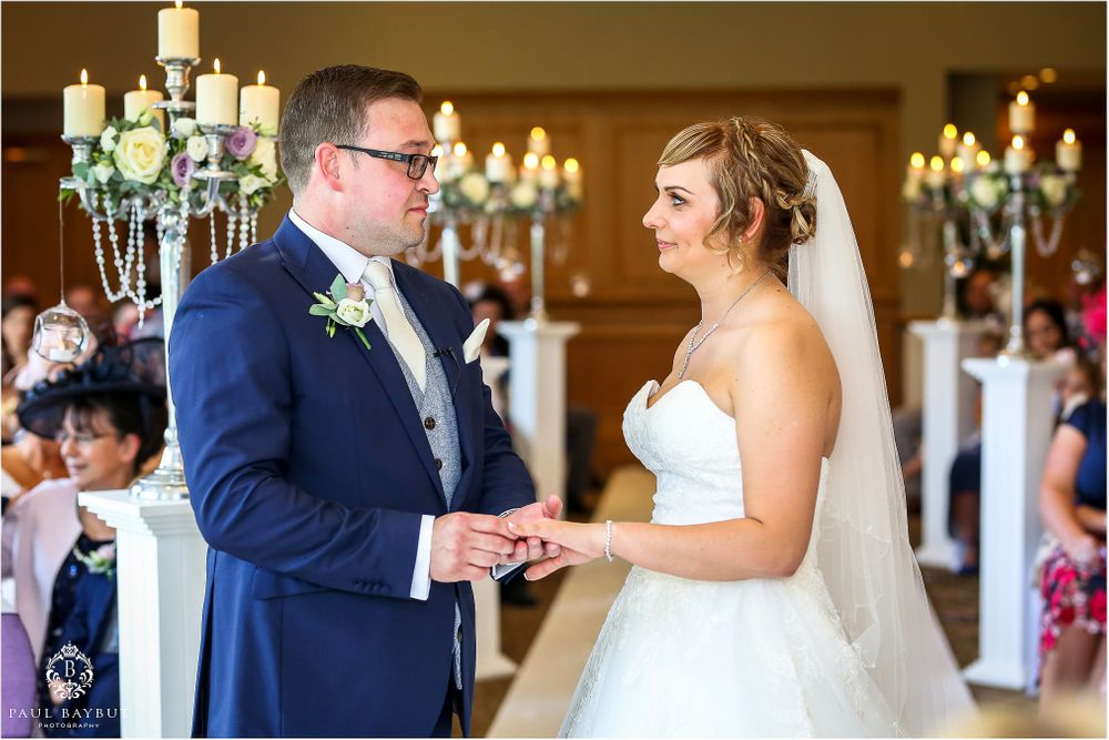Elegant wedding ceremony with chandelier lighting as couple exchanges rings at the altar.