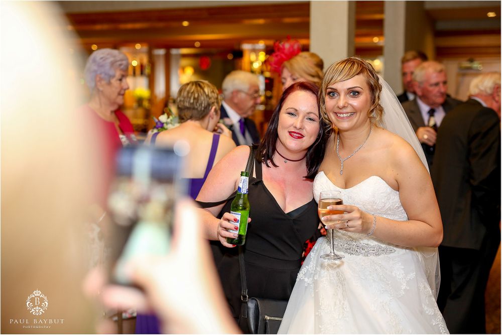 Wedding reception guests enjoying drinks and laughter during a candid moment at the celebration.
