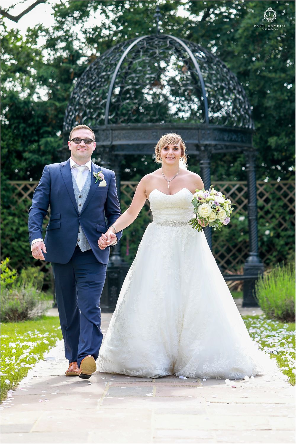 Elegant couple walking hand in hand under decorative garden archway during wedding.